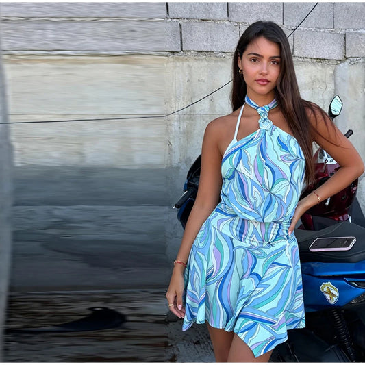 Woman in a blue patterned dress standing next to a motorcycle against a gray wall.