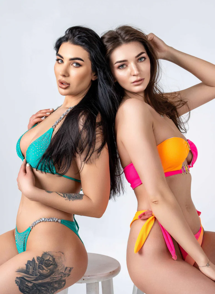 Two models. The right wearing the Italia Couture 'Mae' Bikini Swimsuit in a strapless style with bright pink and orange hues and crystal embellishments.