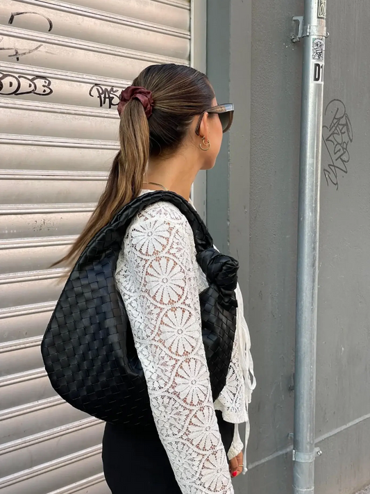 Woman with a black woven bag standing against a gray wall.