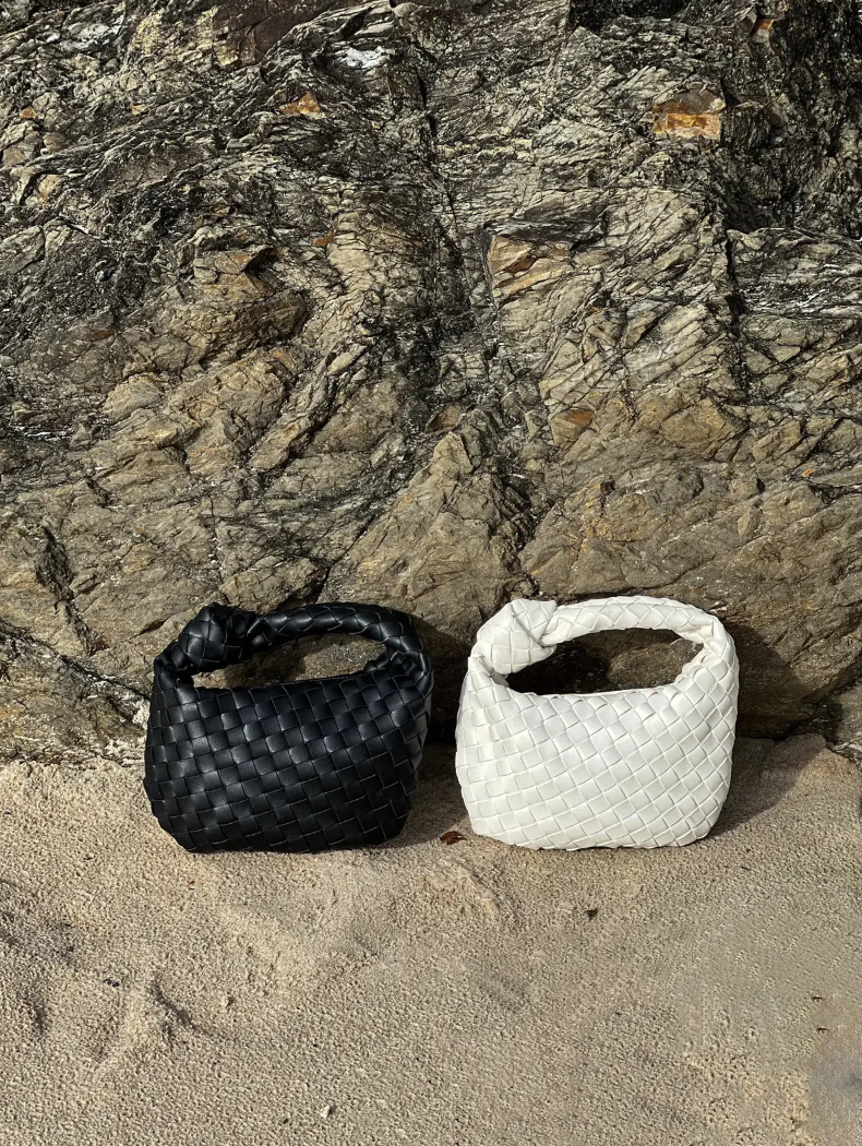 Two woven bags, one black and one white, on a sandy surface with a rocky background.