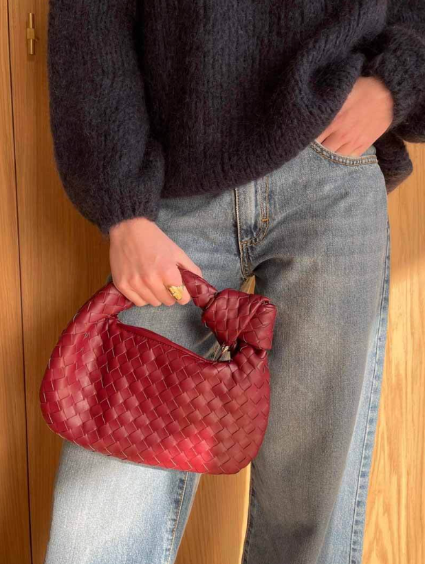 Person holding a red woven handbag against a wooden background