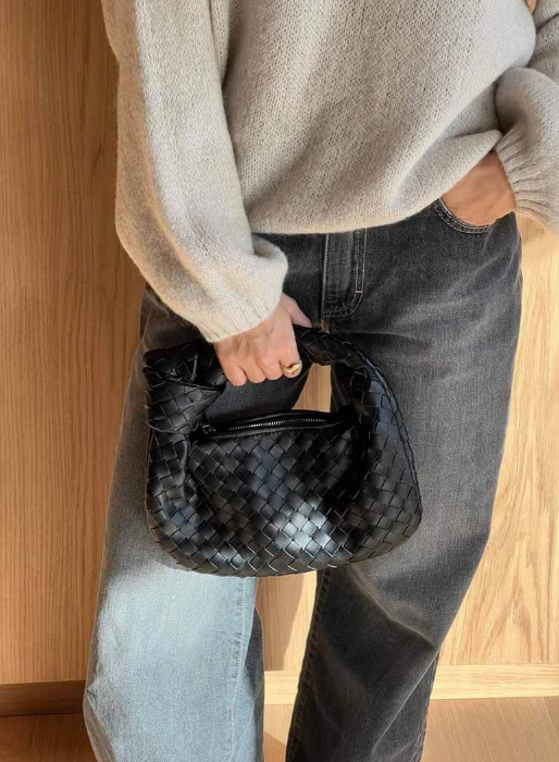 Person holding a black woven handbag with a neutral background