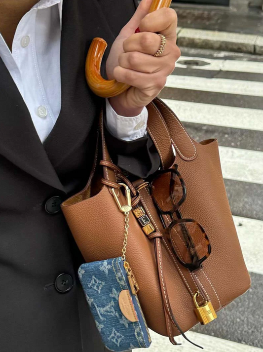 Brown leather handbag with a wooden handle, glasses, and a blue cardholder with gold accents.