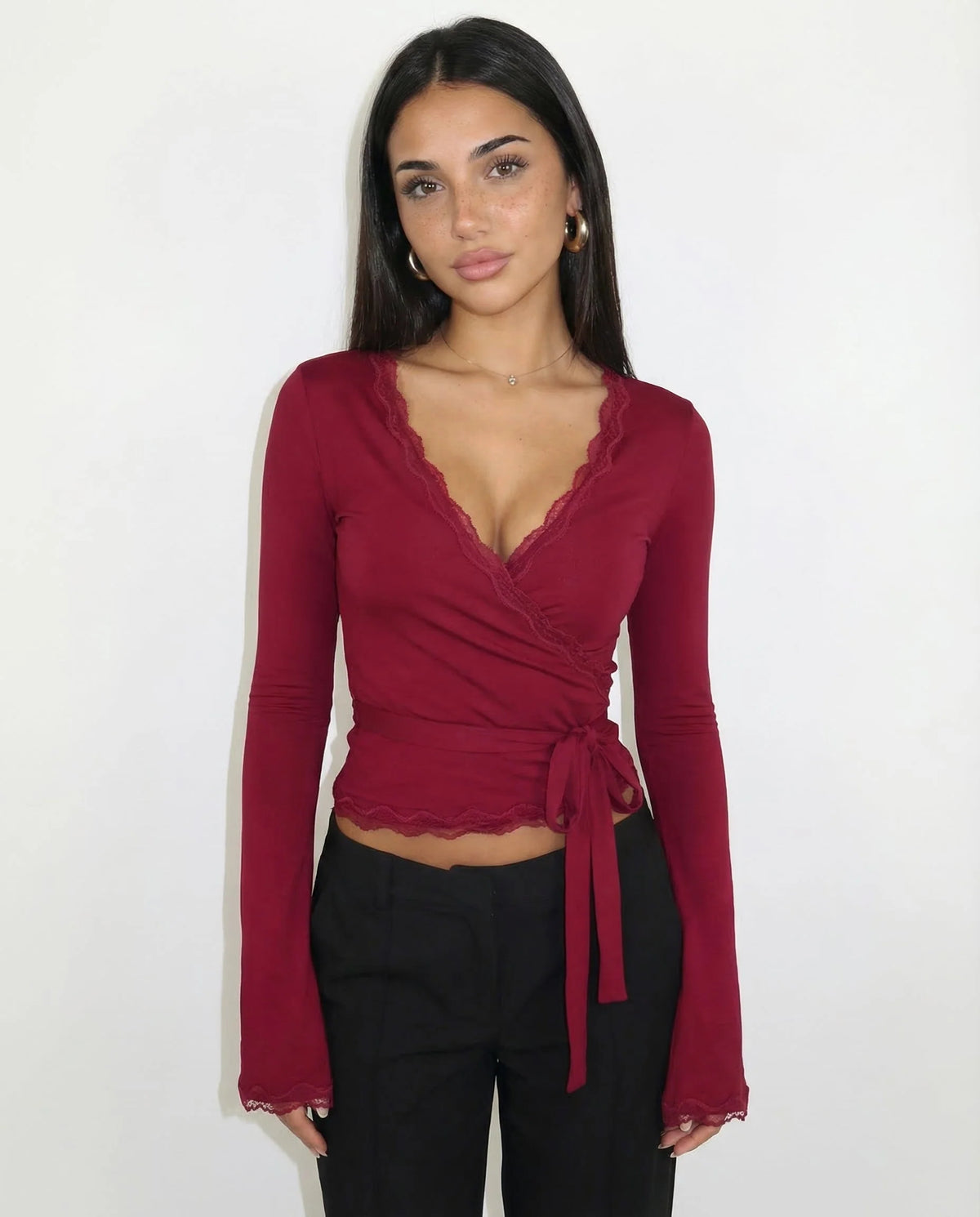 Woman wearing a burgundy long-sleeve top with a tie detail against a white background
