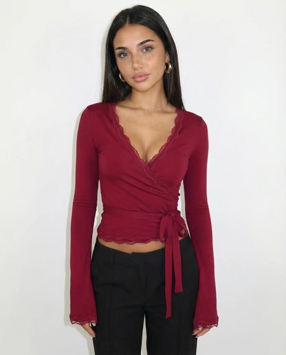 Woman wearing a burgundy long-sleeve top with a tie detail against a white background