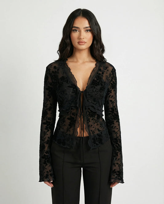 Woman wearing a black floral lace top with a plain background