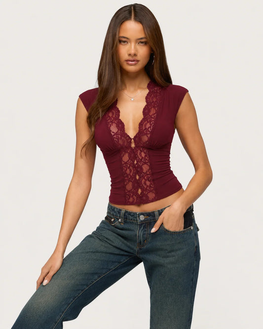 Woman wearing a burgundy lace top and blue jeans on a plain background