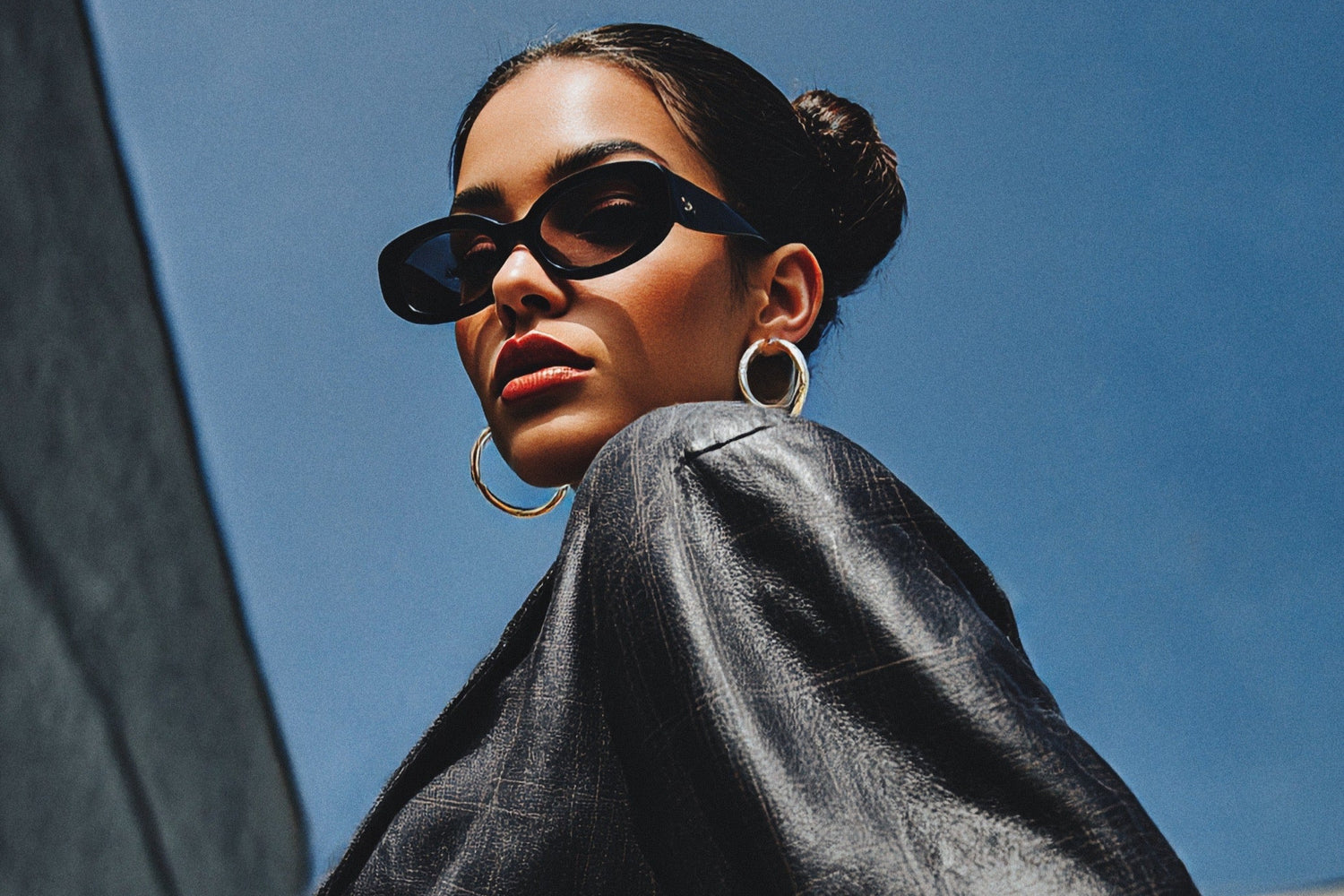 Woman wearing sunglasses and a black jacket against a blue sky.