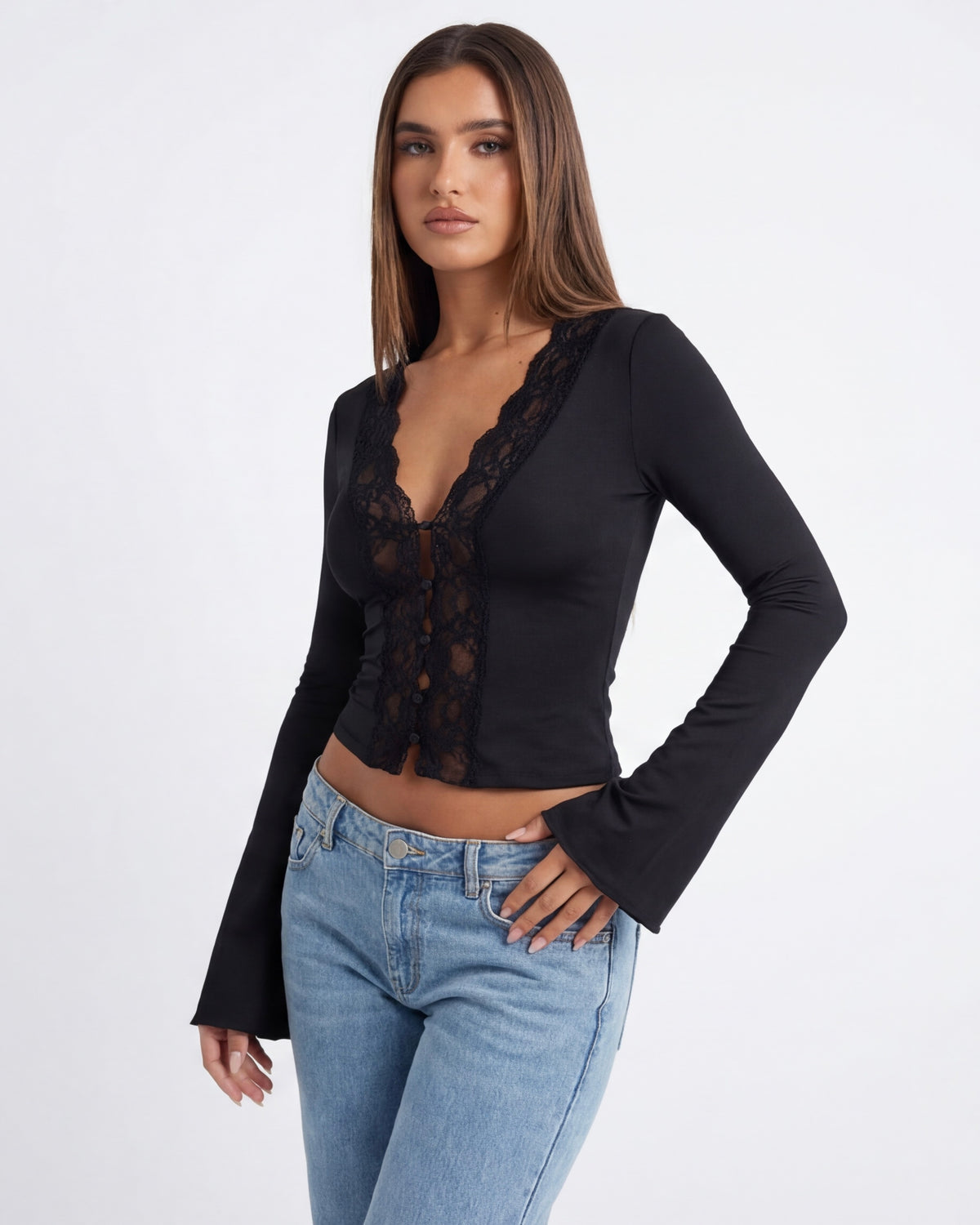 Woman wearing a black long-sleeve top with lace details and light blue jeans on a white background