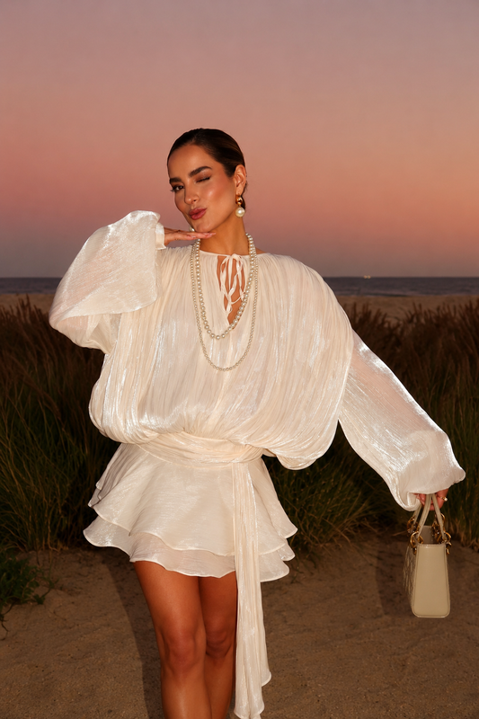 Beige apricot ruffled mini dress worn by a woman standing in a field at sunset