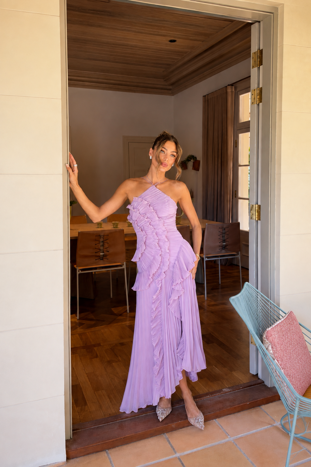 A woman models a lavender ruffled maxi dress in a doorway, with a dining room and patio visible in the background.