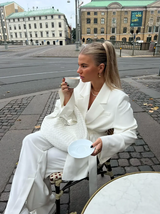 Woman in a white outfit with a white woven bag sitting outdoors in an urban setting