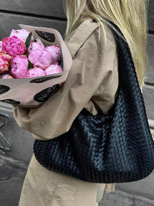 Person holding a bouquet of pink flowers and a black woven bag.