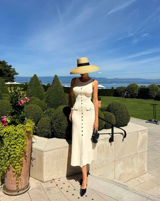 Woman in a white dress and sun hat standing in a garden with ocean view