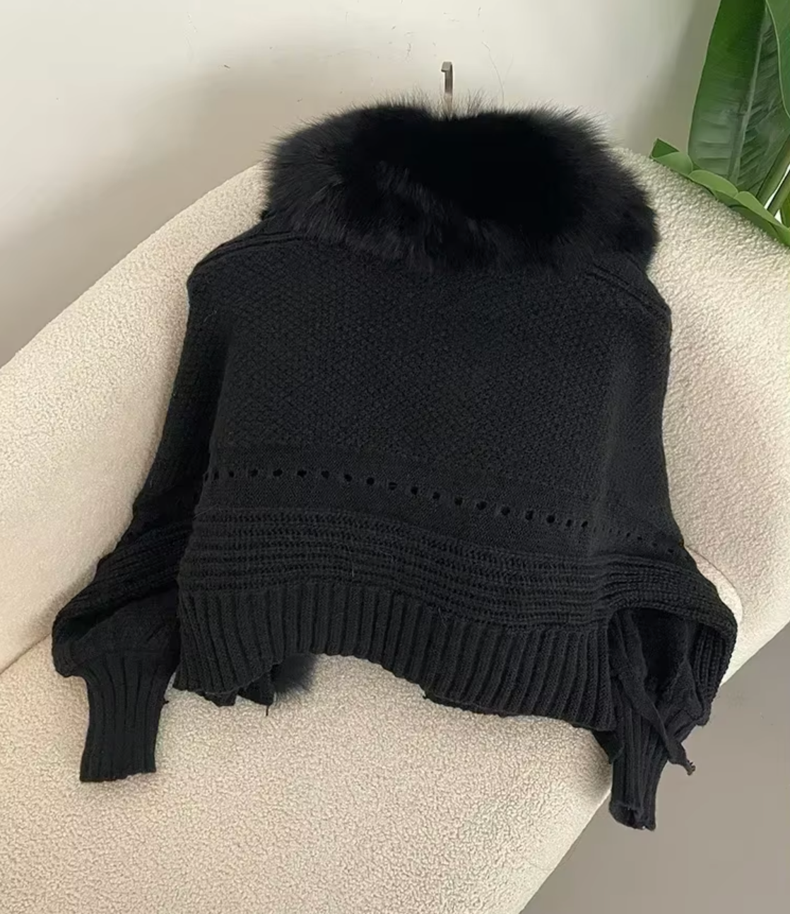 Black knitted sweater with fur collar on a white surface