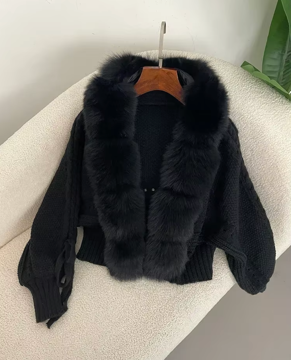 Black fur jacket with a hood on a beige surface