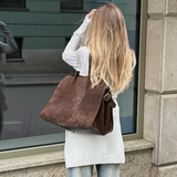 Woman holding a brown leather bag in front of a window