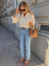 Woman in a white shirt and light blue jeans standing on a sidewalk.